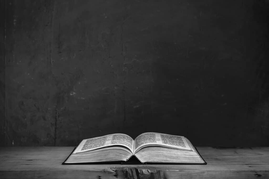 Open bible on a red old wooden table. Beautiful green wall background.